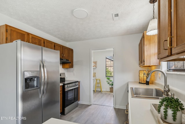 kitchen with stainless steel appliances, sink, pendant lighting, and light hardwood / wood-style floors