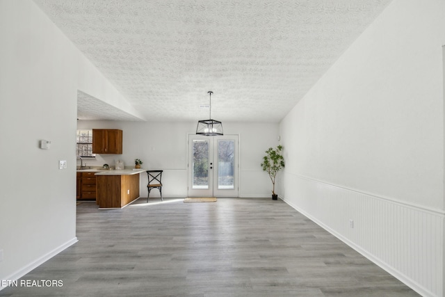 unfurnished dining area with lofted ceiling, a textured ceiling, light wood-type flooring, and french doors