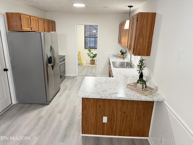 kitchen featuring sink, decorative light fixtures, a textured ceiling, light wood-type flooring, and stainless steel appliances