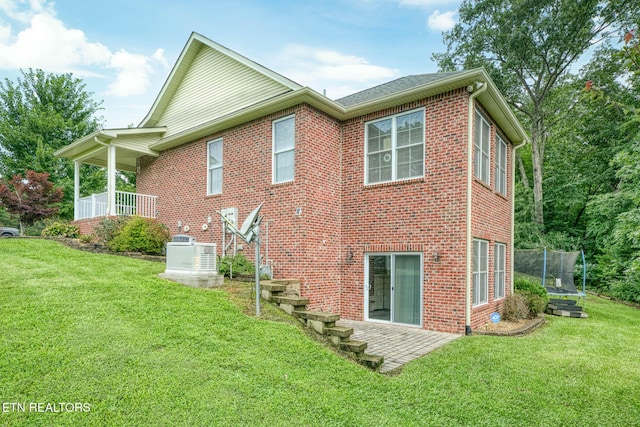 rear view of property with a trampoline, a lawn, and a patio