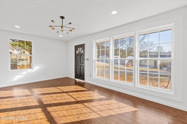 unfurnished room with an inviting chandelier, a healthy amount of sunlight, and hardwood / wood-style floors