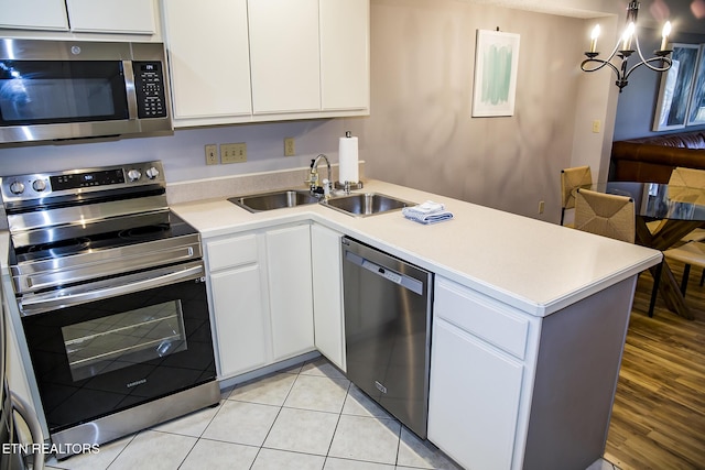 kitchen with sink, light tile patterned floors, stainless steel appliances, white cabinets, and a chandelier