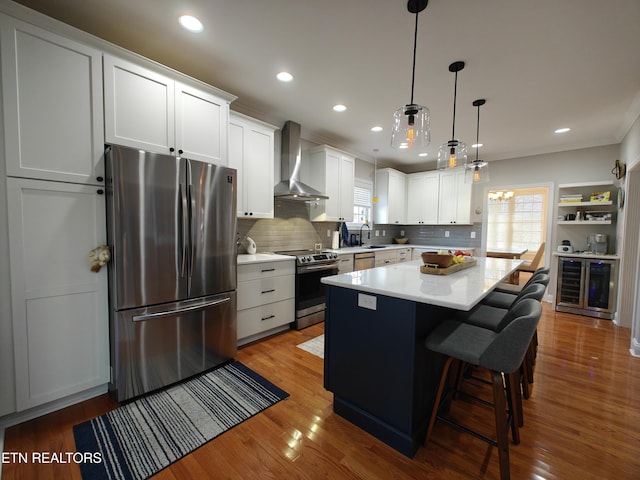 kitchen with pendant lighting, white cabinets, stainless steel appliances, and wall chimney range hood