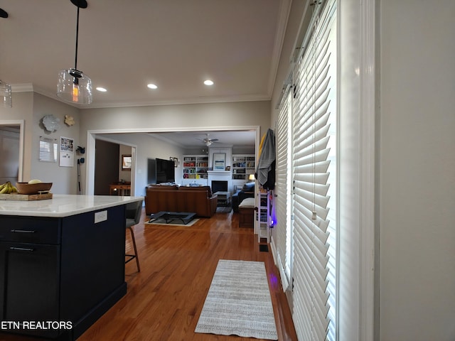 kitchen with dark wood-type flooring, a kitchen bar, ornamental molding, pendant lighting, and ceiling fan