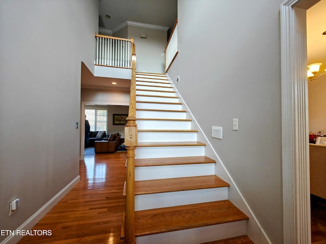 stairs featuring a high ceiling, ornamental molding, and hardwood / wood-style floors