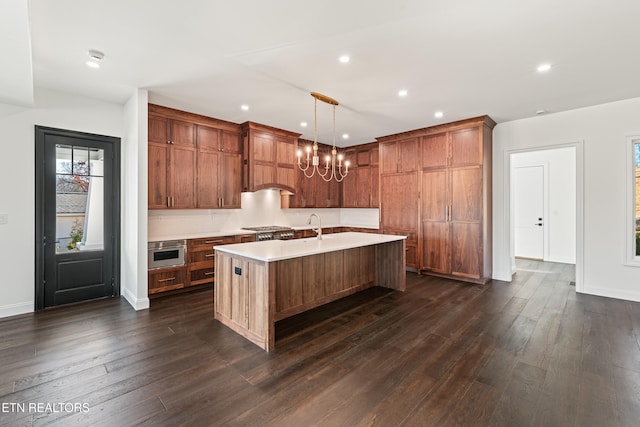 kitchen featuring sink, an inviting chandelier, decorative light fixtures, a center island with sink, and dark hardwood / wood-style floors