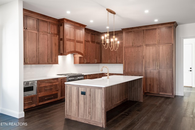 kitchen featuring appliances with stainless steel finishes, pendant lighting, dark hardwood / wood-style flooring, a center island with sink, and an inviting chandelier