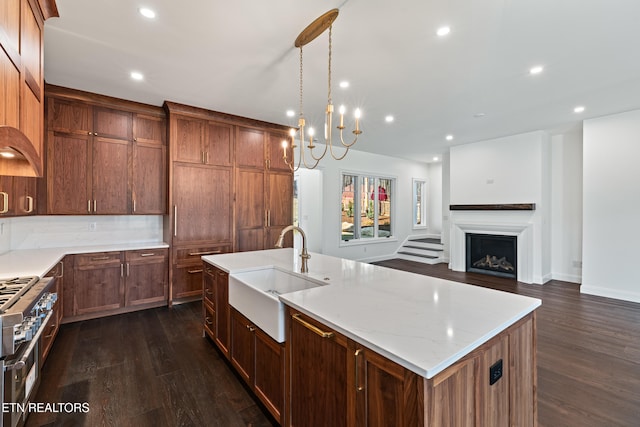 kitchen with decorative light fixtures, sink, high end range, dark wood-type flooring, and a center island with sink