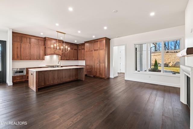 kitchen featuring dark hardwood / wood-style flooring, hanging light fixtures, oven, and an island with sink