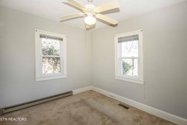 empty room with carpet floors, a baseboard heating unit, ceiling fan, and a healthy amount of sunlight