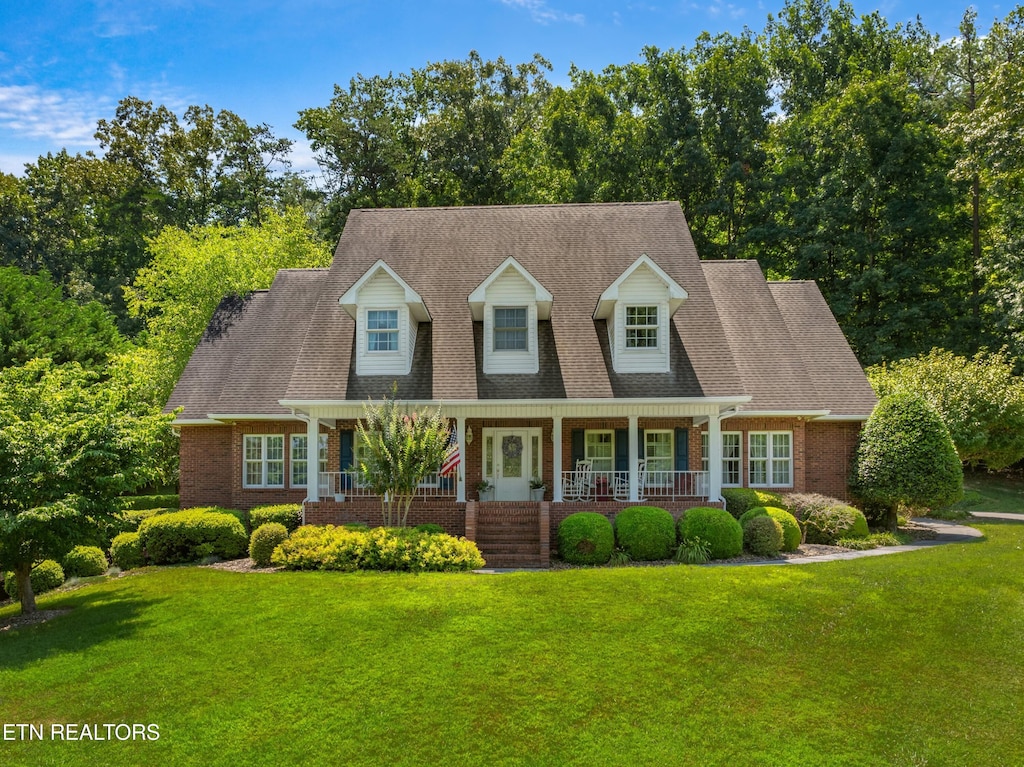 cape cod house with a front yard and covered porch