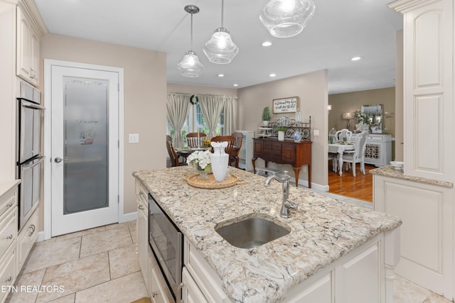 kitchen featuring a kitchen island with sink, hanging light fixtures, light stone countertops, white cabinets, and sink