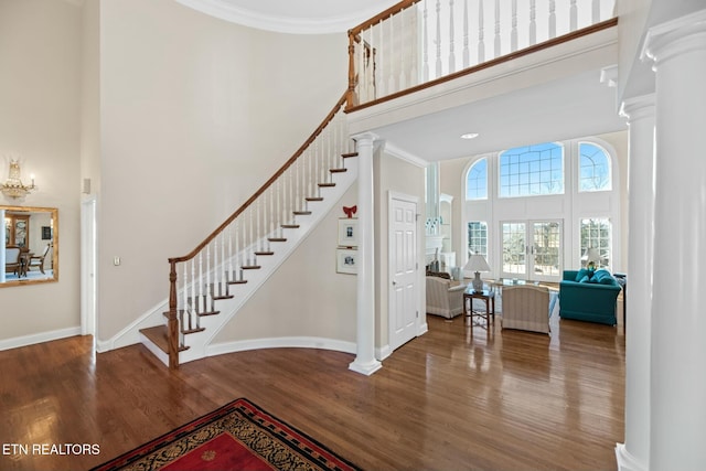 foyer entrance with a towering ceiling, ornamental molding, hardwood / wood-style flooring, and ornate columns