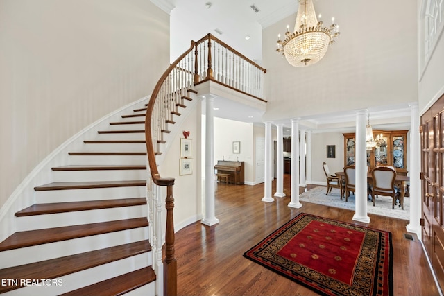 foyer entrance featuring ornamental molding, dark hardwood / wood-style floors, a notable chandelier, a towering ceiling, and decorative columns