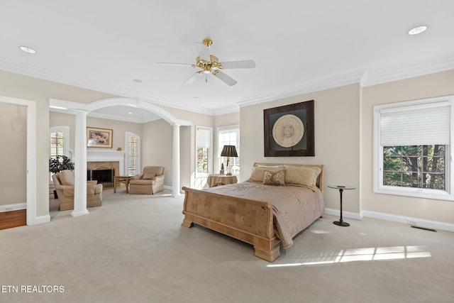 carpeted bedroom with decorative columns, a tile fireplace, ornamental molding, and ceiling fan