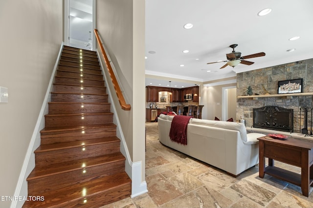 staircase with crown molding, ceiling fan, and a fireplace