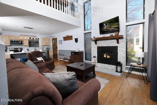 living room with light hardwood / wood-style floors, a textured ceiling, a towering ceiling, and a fireplace