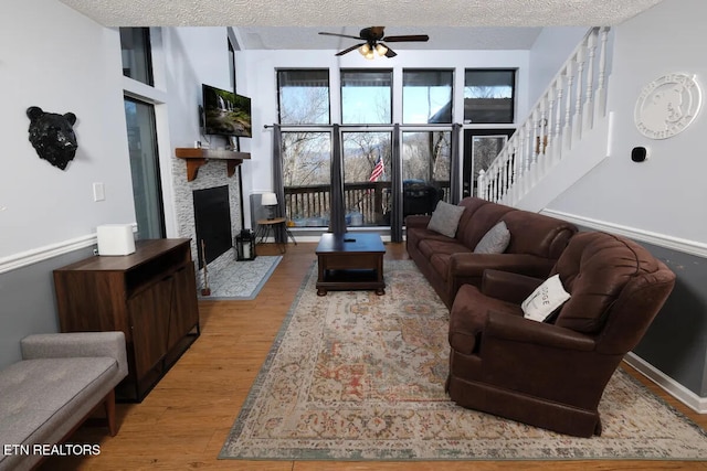 1580 Zermatt Dr, Gatlinburg, TN 37738 - living room featuring a textured ceiling, ceiling fan, a stone fireplace, and light wood-type flooring