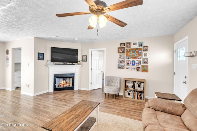 living room with ceiling fan, light wood-type flooring, and a textured ceiling