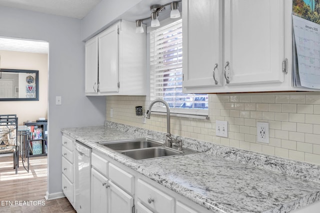 kitchen featuring white dishwasher, sink, backsplash, and white cabinets