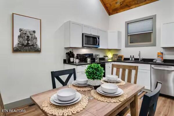 kitchen featuring wood ceiling, appliances with stainless steel finishes, lofted ceiling, light hardwood / wood-style flooring, and sink