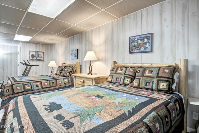 bedroom featuring a paneled ceiling and wooden walls