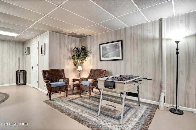 sitting room featuring wood walls, concrete floors, and a drop ceiling