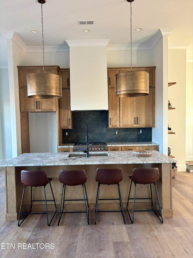 kitchen featuring decorative light fixtures, light hardwood / wood-style flooring, sink, and a center island with sink