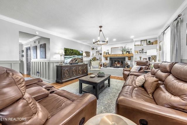 living room featuring a fireplace, a notable chandelier, crown molding, light hardwood / wood-style flooring, and built in features