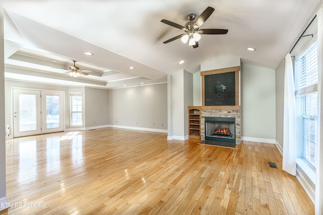 unfurnished living room with a raised ceiling, vaulted ceiling, ceiling fan, and light hardwood / wood-style flooring