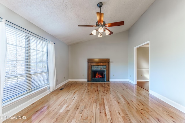 unfurnished living room with lofted ceiling, ceiling fan, a fireplace, light hardwood / wood-style floors, and a textured ceiling