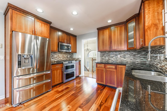 kitchen featuring dark hardwood / wood-style floors, sink, dark stone countertops, stainless steel appliances, and an inviting chandelier