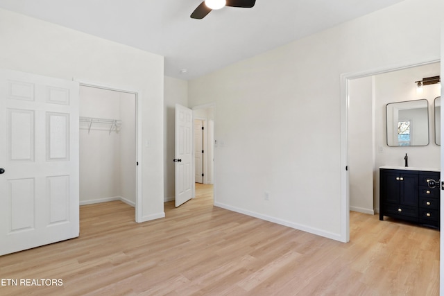 unfurnished bedroom featuring a spacious closet, sink, a closet, ceiling fan, and light hardwood / wood-style flooring