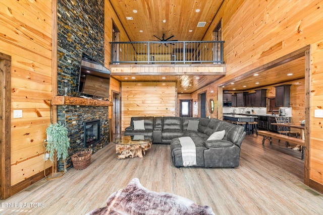 living room featuring a fireplace, wooden walls, a high ceiling, light wood-type flooring, and wooden ceiling