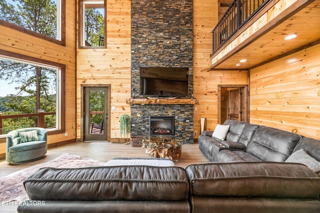 living room featuring a stone fireplace, wooden walls, a towering ceiling, and hardwood / wood-style flooring