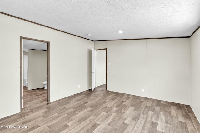 empty room featuring crown molding, light hardwood / wood-style floors, and a textured ceiling