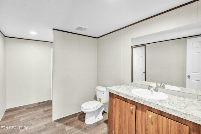 bathroom featuring wood-type flooring, vanity, crown molding, and toilet