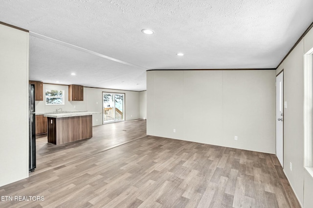 unfurnished living room with crown molding, a textured ceiling, and light hardwood / wood-style flooring