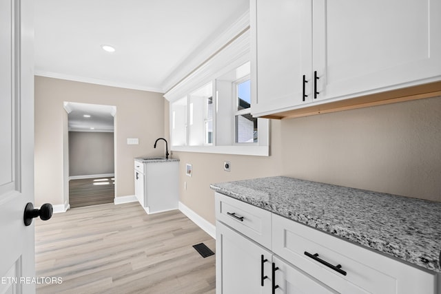 kitchen featuring white cabinetry, sink, crown molding, and light stone counters