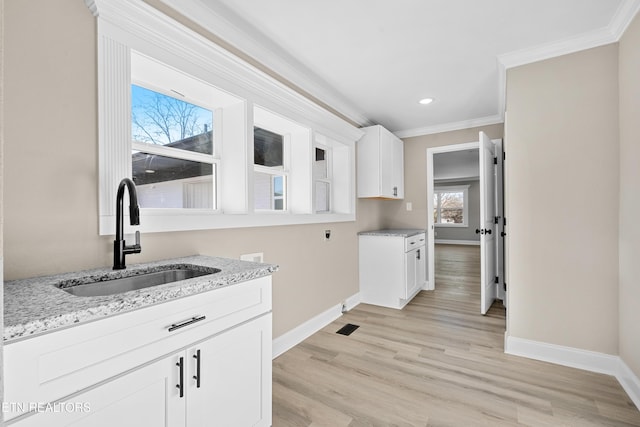 interior space featuring sink, crown molding, white cabinetry, light stone counters, and light hardwood / wood-style floors