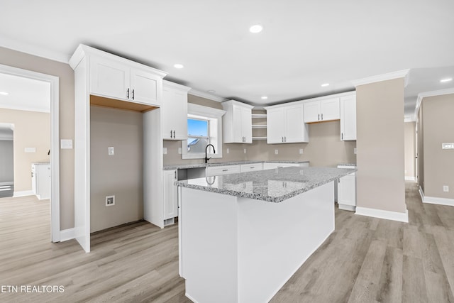 kitchen featuring white cabinetry, a center island, light stone countertops, and light hardwood / wood-style floors