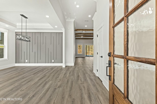 hall with a raised ceiling, ornamental molding, and wood-type flooring