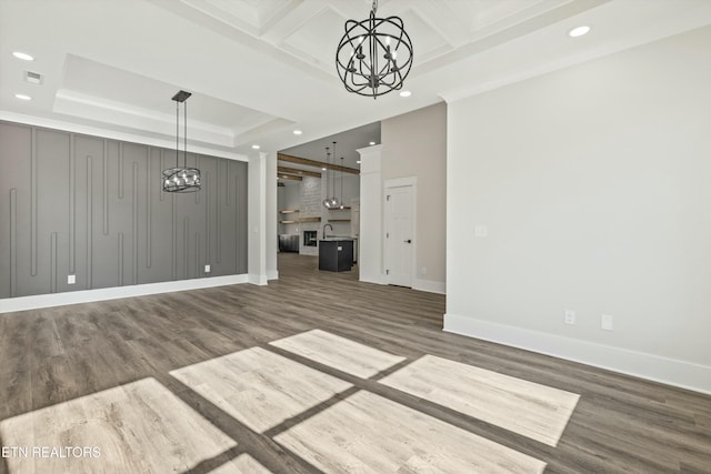 unfurnished living room featuring sink, dark wood-type flooring, a tray ceiling, coffered ceiling, and an inviting chandelier