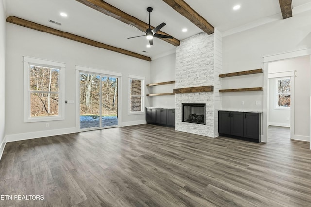 unfurnished living room with ceiling fan, beamed ceiling, dark hardwood / wood-style flooring, and a stone fireplace