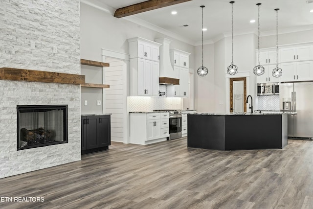 kitchen featuring pendant lighting, white cabinets, a stone fireplace, a kitchen island with sink, and stainless steel appliances