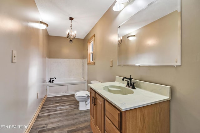 bathroom featuring wood-type flooring, vanity, toilet, a chandelier, and a bathing tub