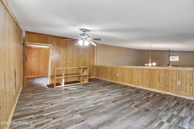 spare room with dark hardwood / wood-style flooring, ceiling fan with notable chandelier, wooden walls, and a textured ceiling