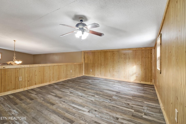 empty room with dark wood-type flooring, ceiling fan with notable chandelier, and wooden walls