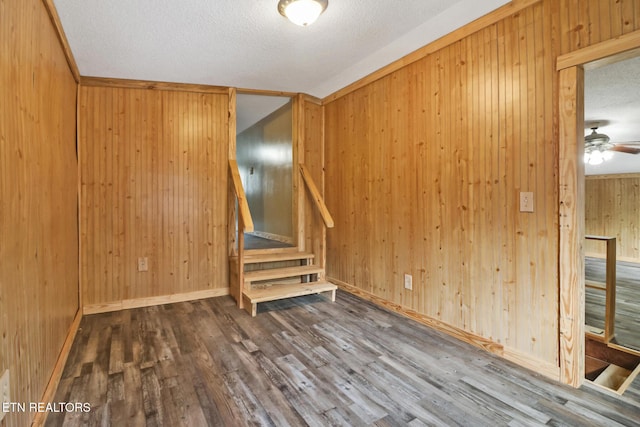 unfurnished living room featuring a textured ceiling, wood walls, hardwood / wood-style floors, and ceiling fan