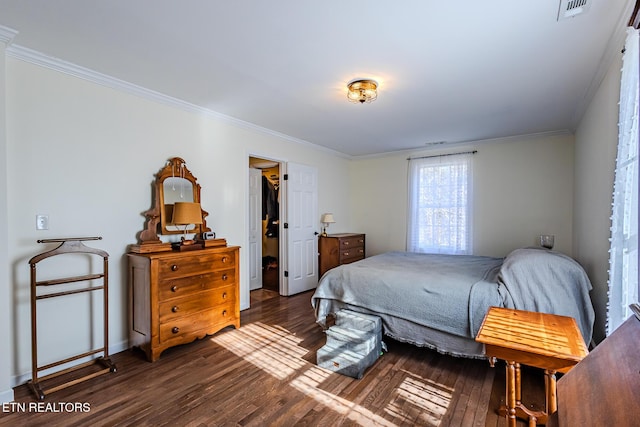 bedroom featuring dark wood-type flooring, a walk in closet, crown molding, and a closet